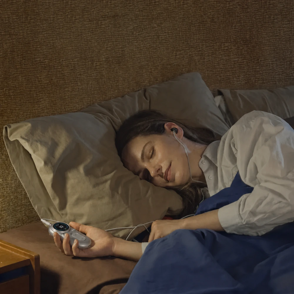 Person using the silver ZenoWell Luna for ear-based vagus nerve stimulation at bedtime